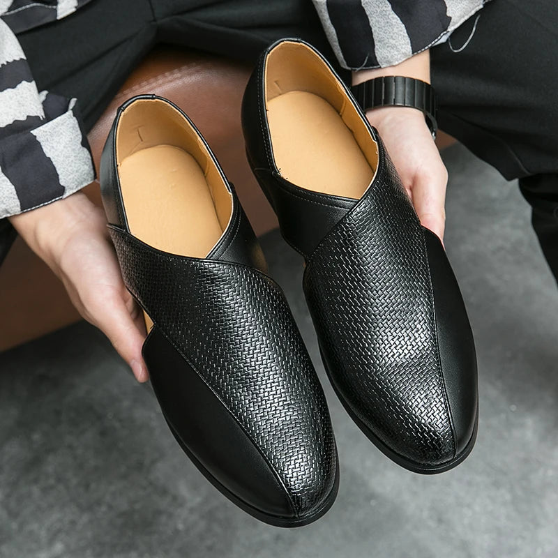 Black textured loafers held by a person on a gray surface