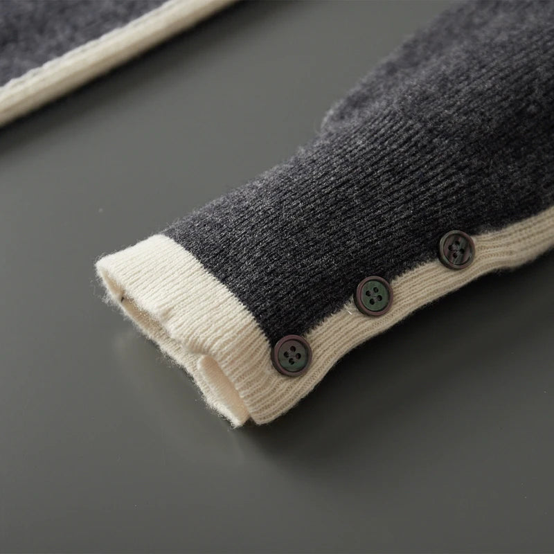 Close-up of a dark gray sweater with beige cuffs and buttons on a dark surface