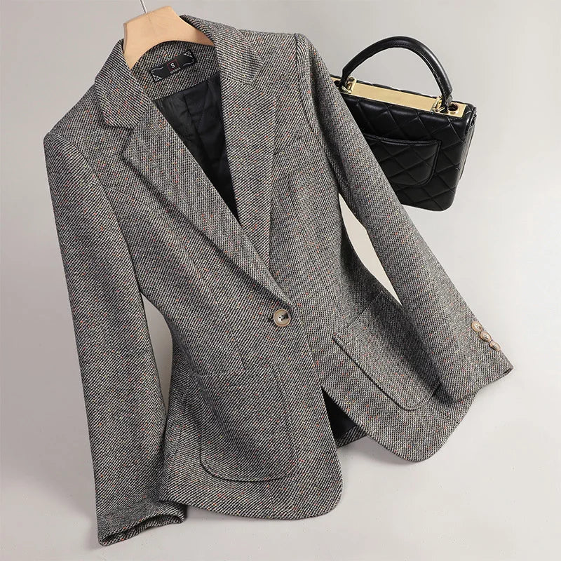 Gray blazer on a hanger with a black handbag on a light gray background