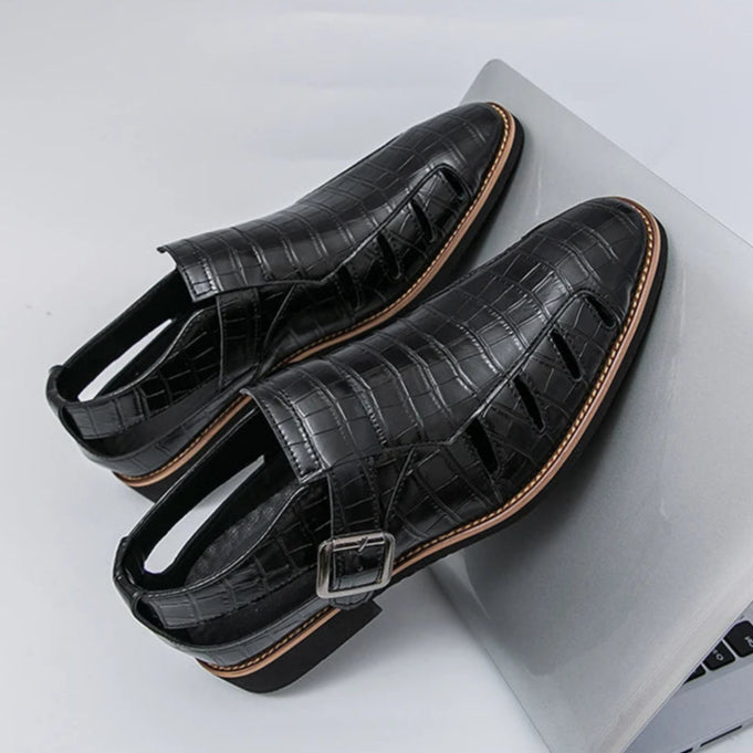 Black leather shoes on a white background with a person wearing yellow sandals on a gray floor.