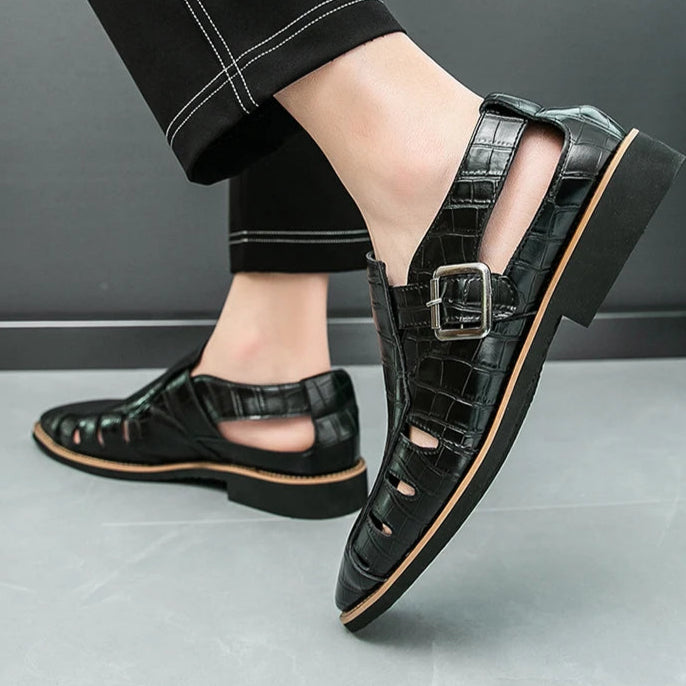 Black leather shoes with buckles worn by a person on a gray floor.