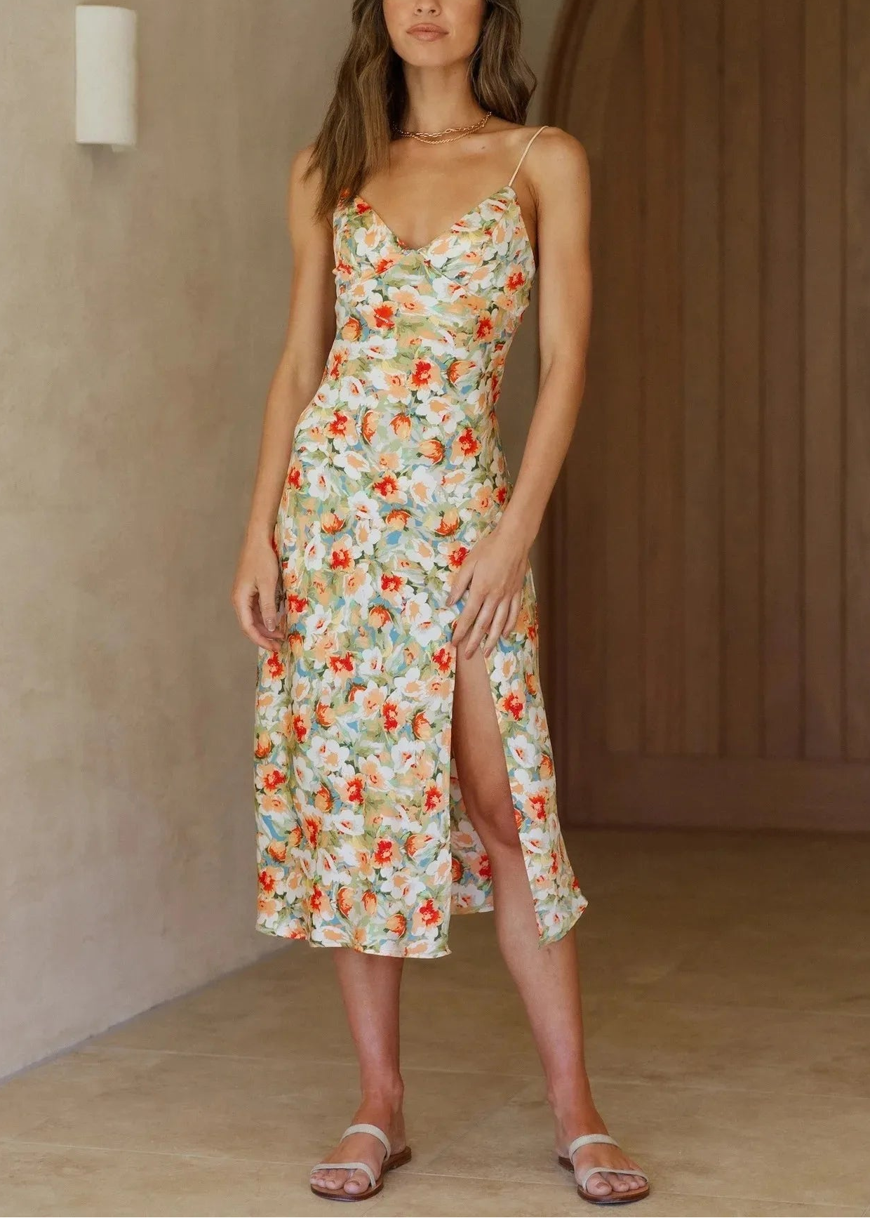 Woman wearing a floral dress standing against a neutral wall.