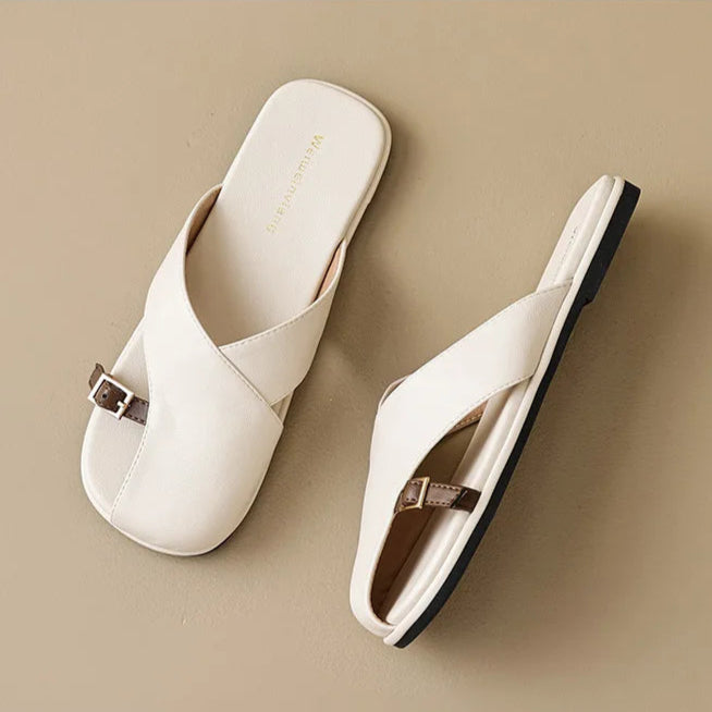 White slippers with a gold buckle on a beige background