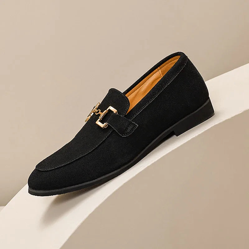 Black loafer shoe with gold buckle on a beige background