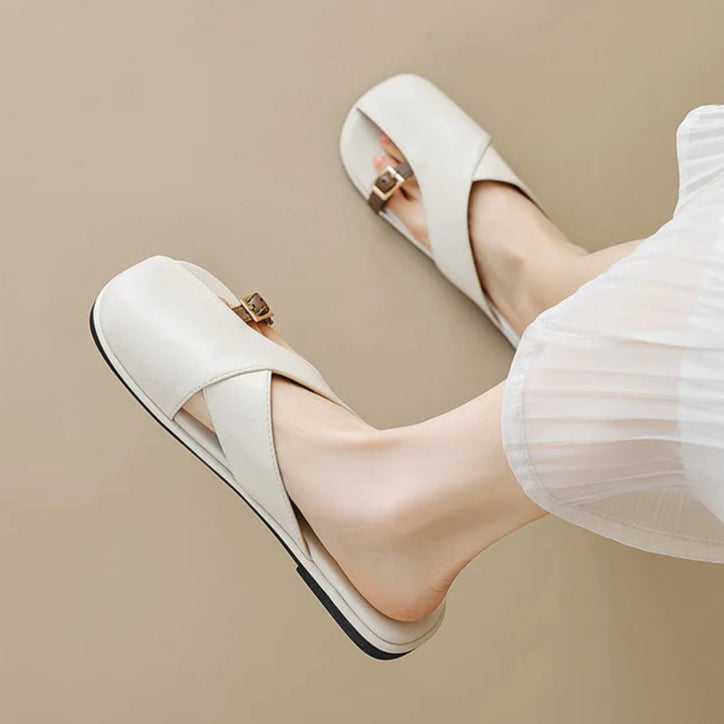 White shoes with gold buckles worn by a person on a beige background