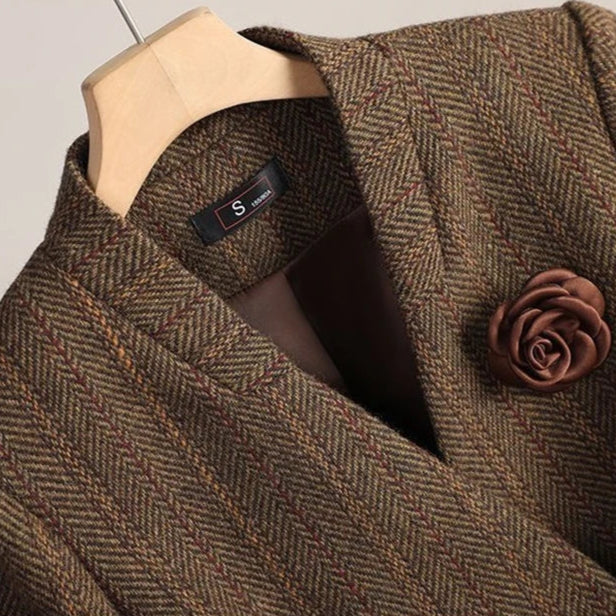 Brown textured coat with a flower pin on a hanger against a neutral background