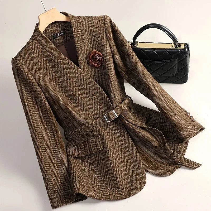 Brown blazer with a belt and black quilted handbag on a light background