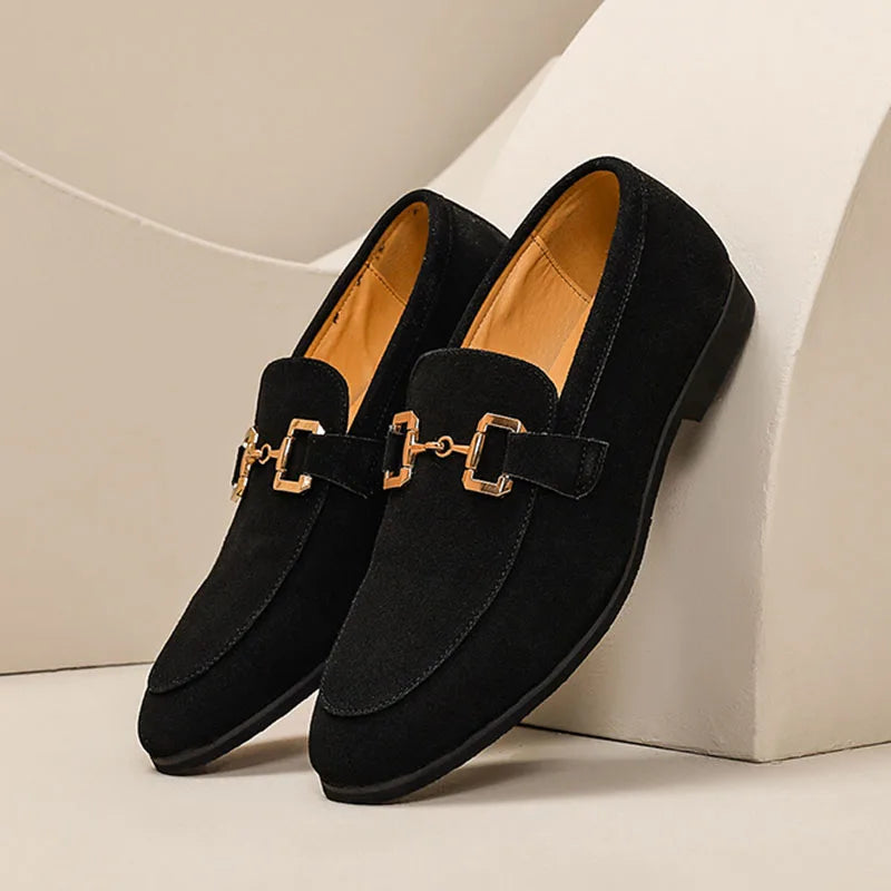 Black loafers with gold buckles on a beige background