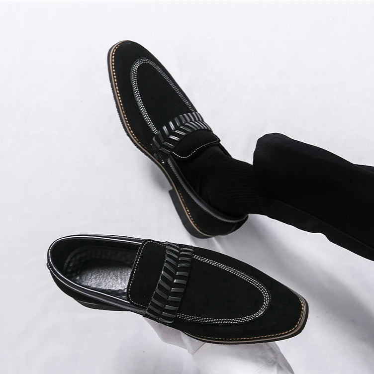 Black loafers with decorative straps worn with black pants on a white background