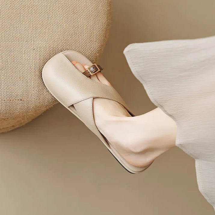 Beige slippers worn with white pants on a beige background