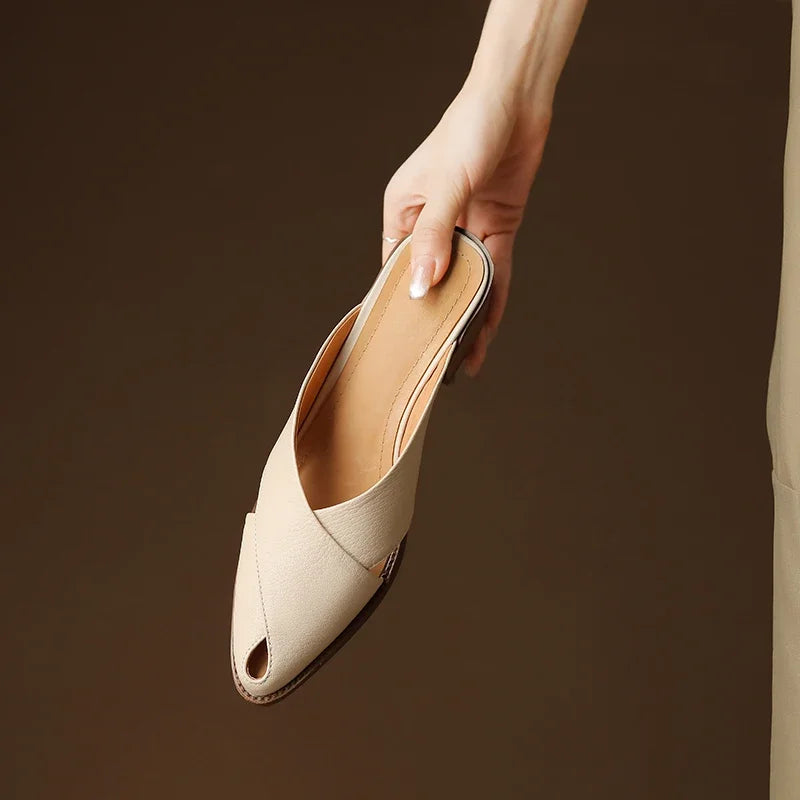 Beige flat shoe held by a hand against a brown background